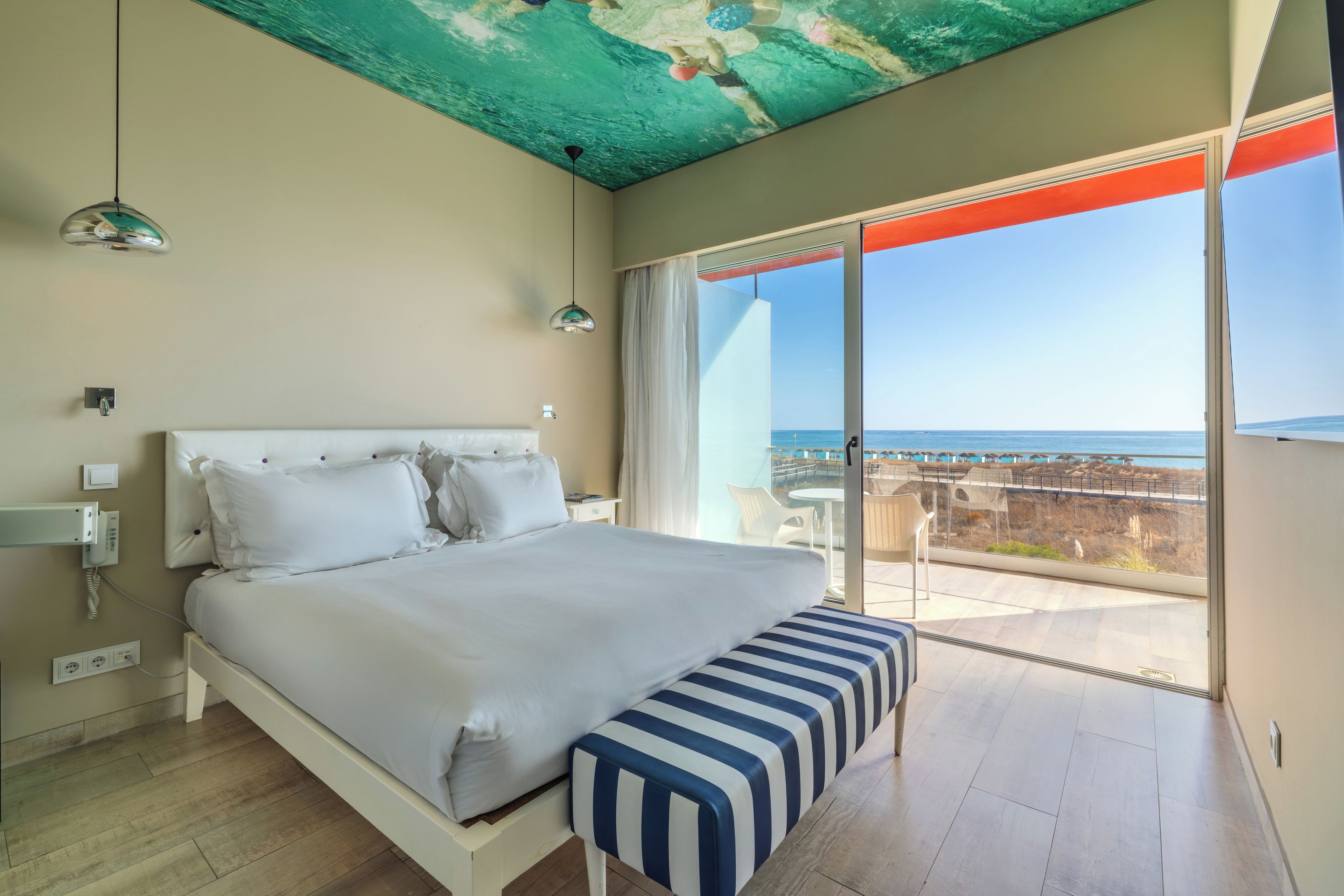 Un dormitorio con una cama, un banco, un techo de diseño único y un balcón con vistas al mar.