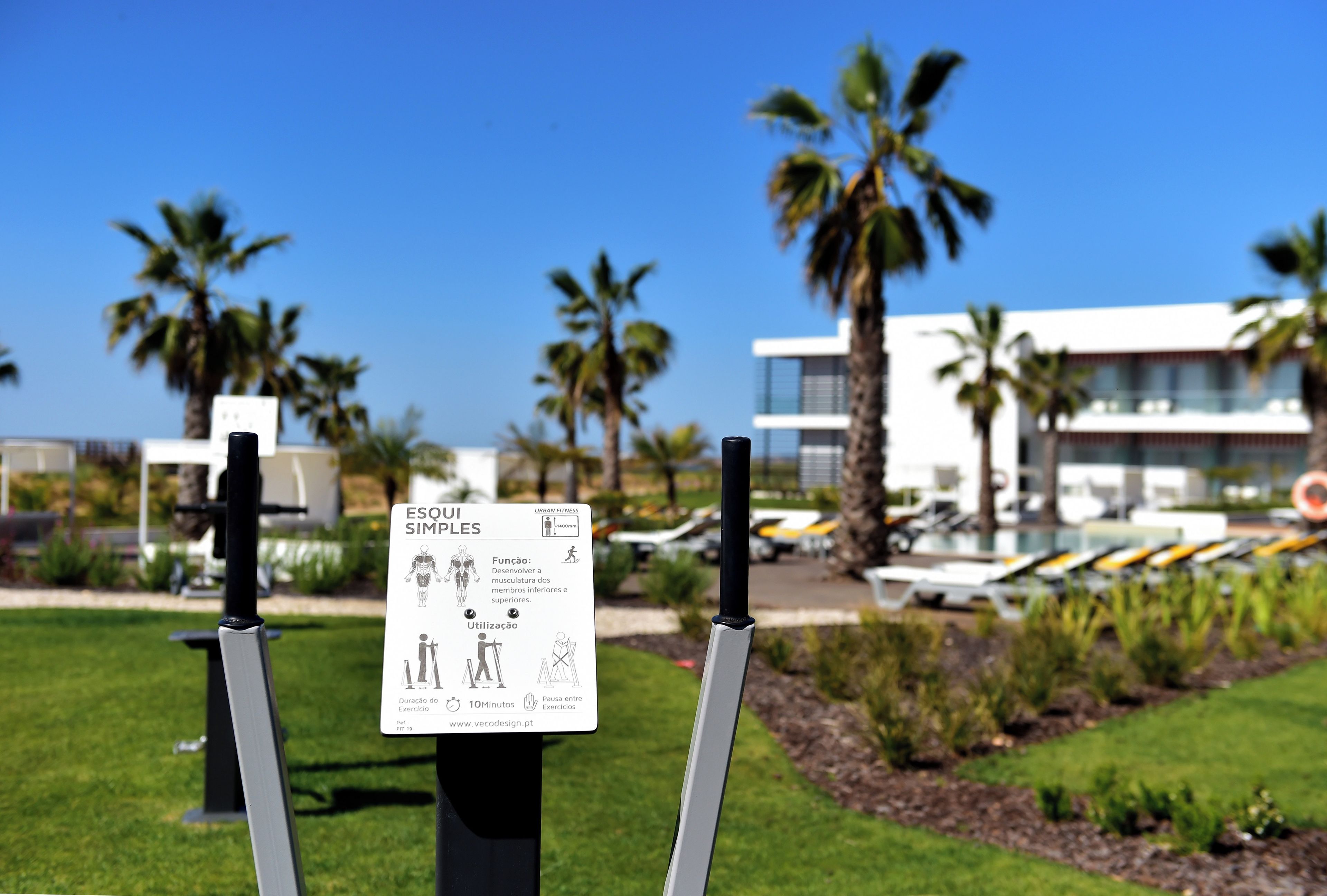 A sign with exercise instructions in a sunny outdoor area with palm trees and a modern building in the background.