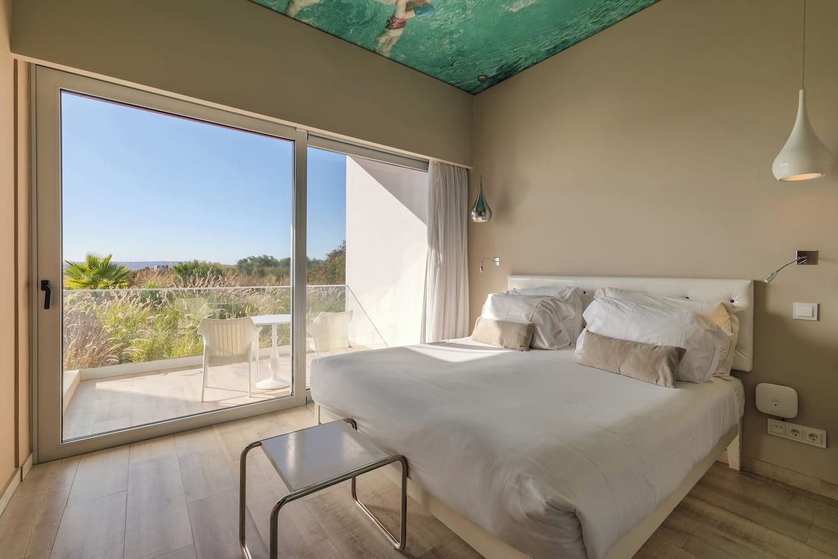 A bedroom with a large bed, a sliding glass door to a balcony, and a ceiling with exposed beams.