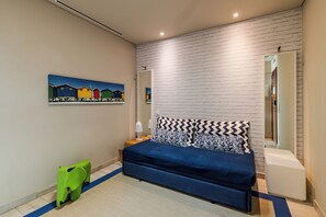 A bedroom with a bed, a nightstand, a lamp, a green chair, a painting, and a white brick wall. - Pestana Alvor South Beach, Premium Suite Hotel (Portimão)