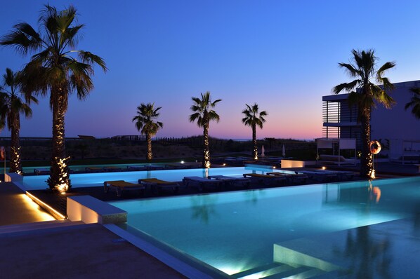 A swimming pool with lounge chairs and palm trees, surrounded by a modern building. - Pestana Alvor South Beach, Premium Suite Hotel (PortimĂŁo)