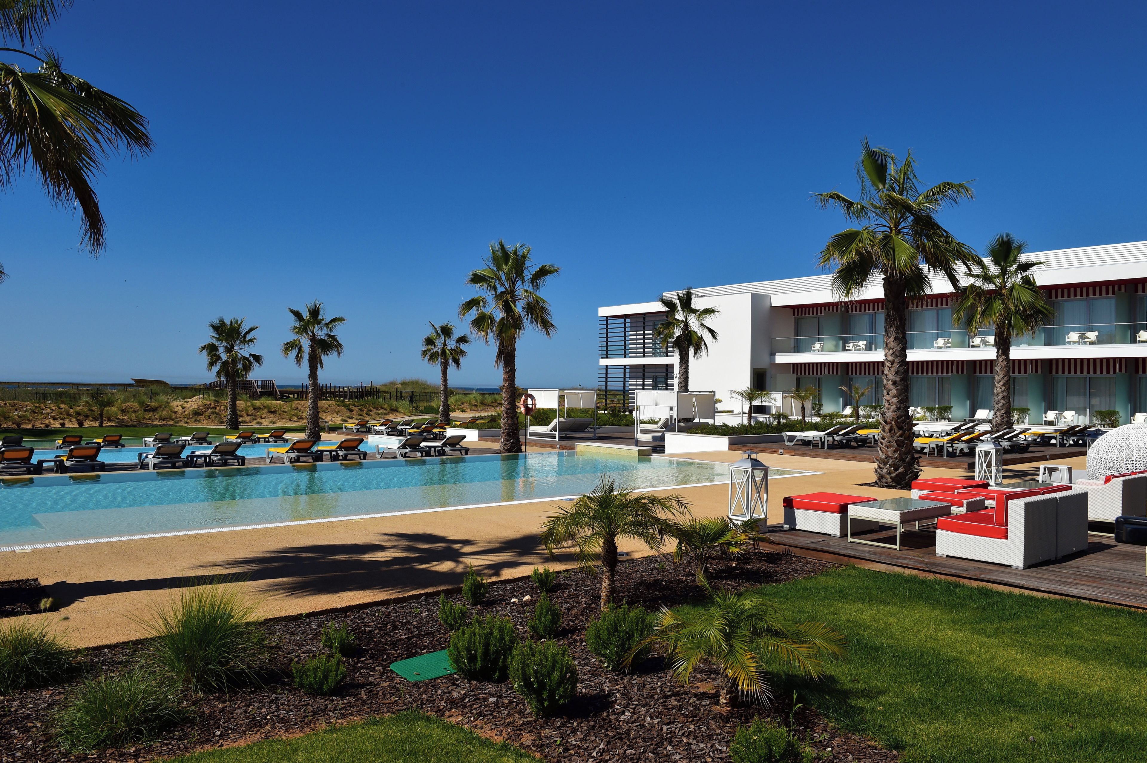 Zona de piscina en un resort, con múltiples sillas de descanso y un edificio grande con balcones.