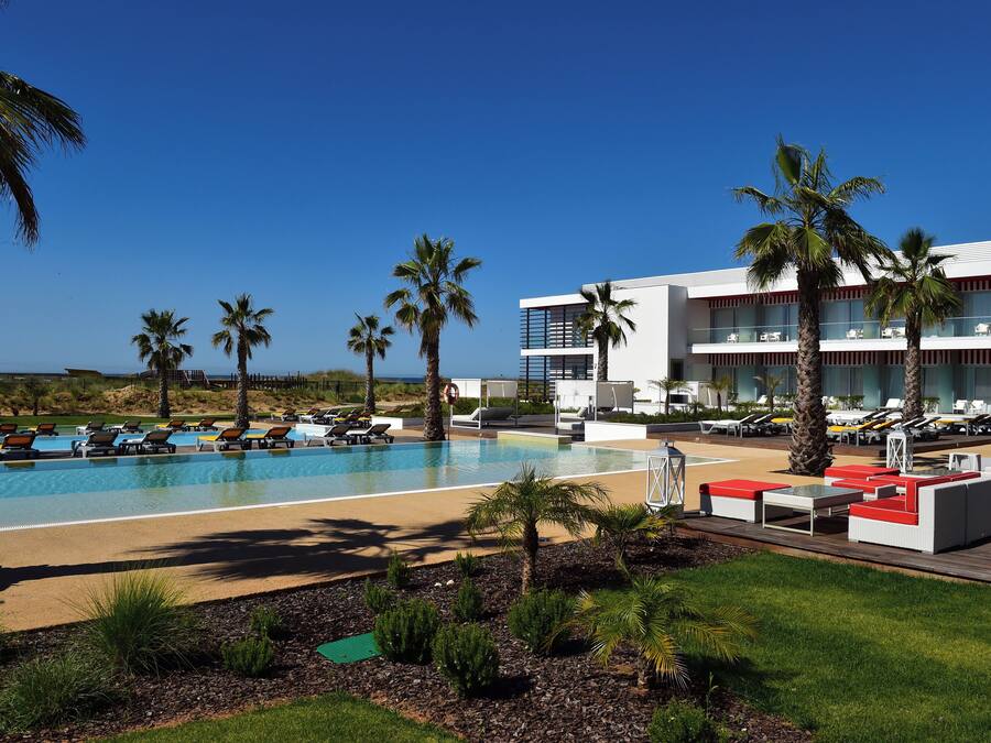 Zona de piscina en un resort, con múltiples sillas de descanso y un edificio grande con balcones.