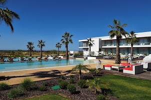 A resort pool area with multiple lounge chairs and a large building with balconies.