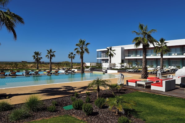 Zona de piscina en un resort, con múltiples sillas de descanso y un edificio grande con balcones.