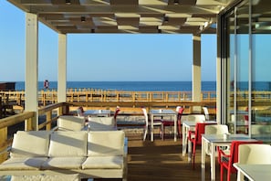 An outdoor seating area with tables and chairs, overlooking a beach and the ocean. - Pestana Alvor South Beach, Premium Suite Hotel (PortimĂŁo)