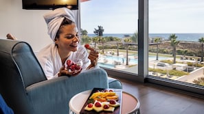 A person relaxing by a window with a view of a pool and the ocean. - Pestana Alvor South Beach, Premium Suite Hotel (PortimĂŁo)