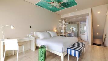Habitació d'hotel amb llit, escriptori, cadira, maleta i zona de dutxa.