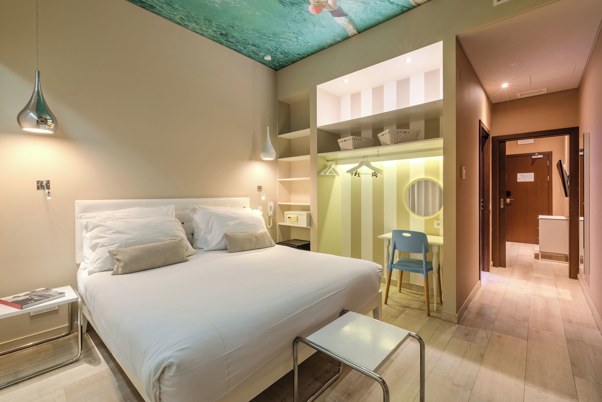 A modern hotel room with a large bed, bedside table, and a small desk area with a chair.