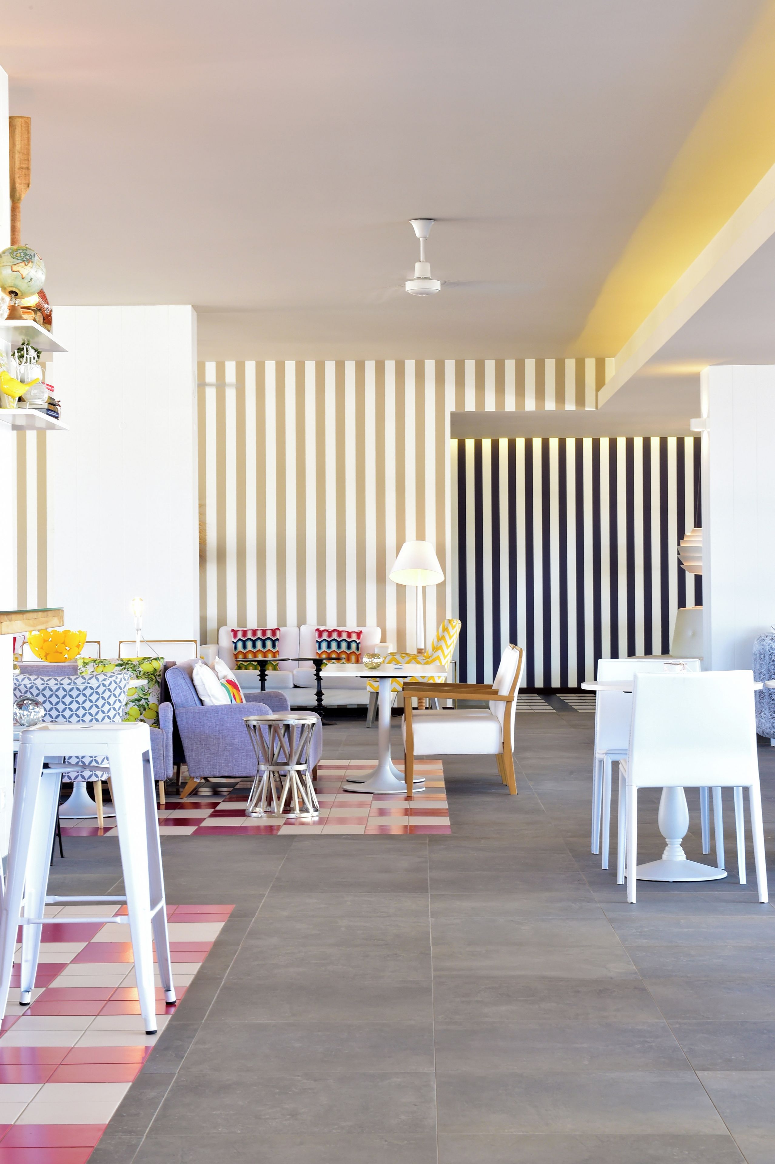 A modern living room with a dining area, featuring striped wallpaper, a ceiling fan, and contemporary furniture.