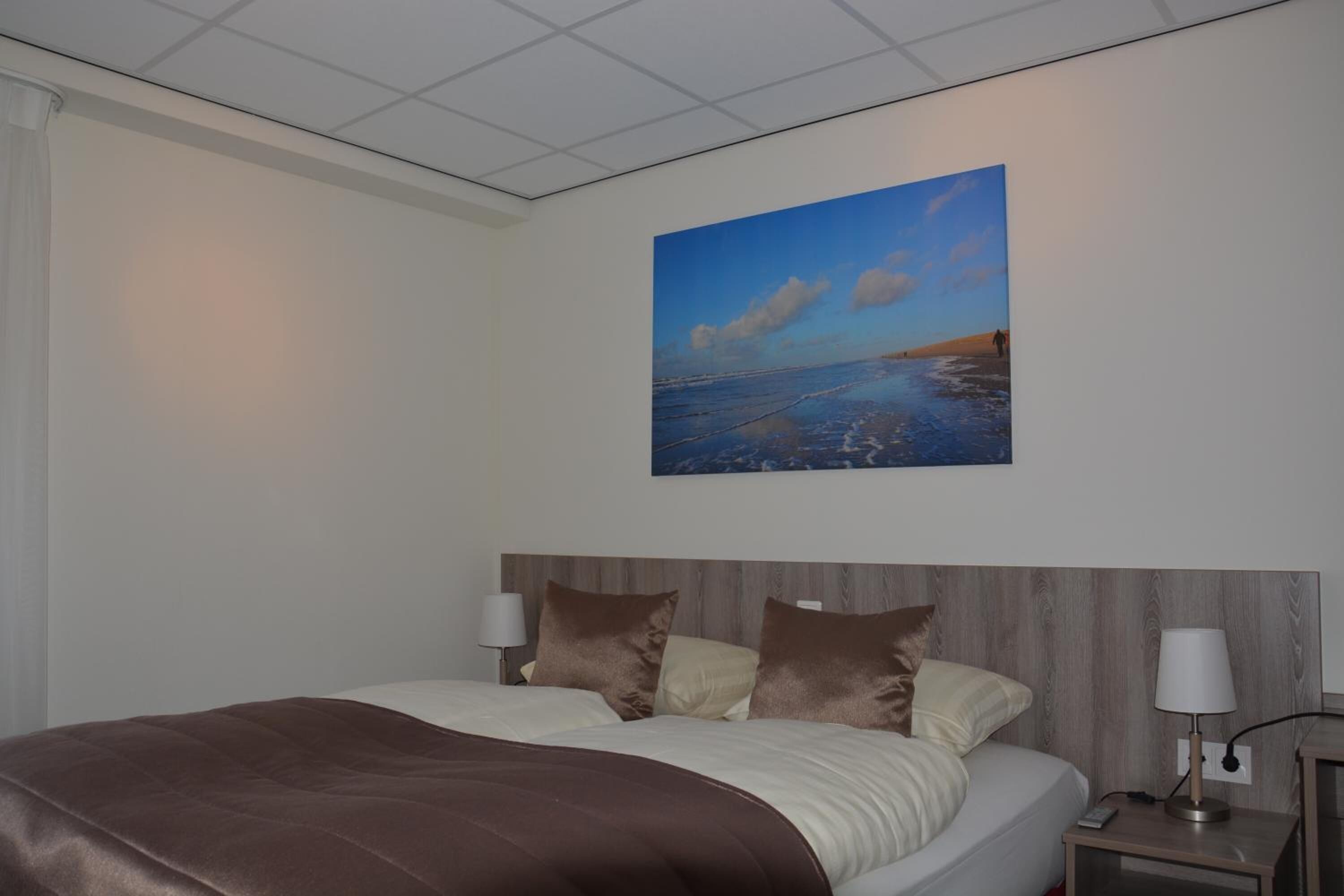 Une chambre d’hôtel avec un grand lit, deux tables de chevet avec des lampes et un tableau représentant une scène de plage au mur.