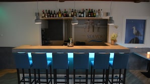 Een bar met een lange toonbank, meerdere krukken en diverse flessen op planken.