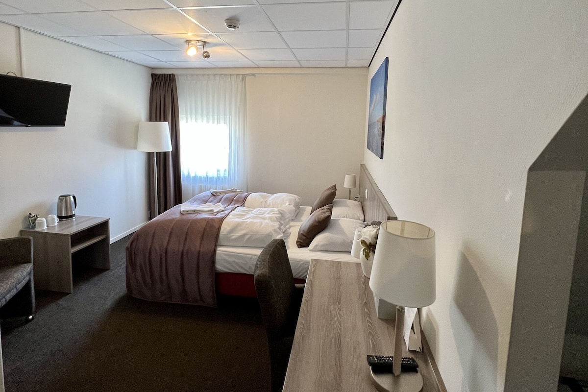 A hotel room with a bed, a desk, a chair, a TV, a lamp, and a coffee maker.