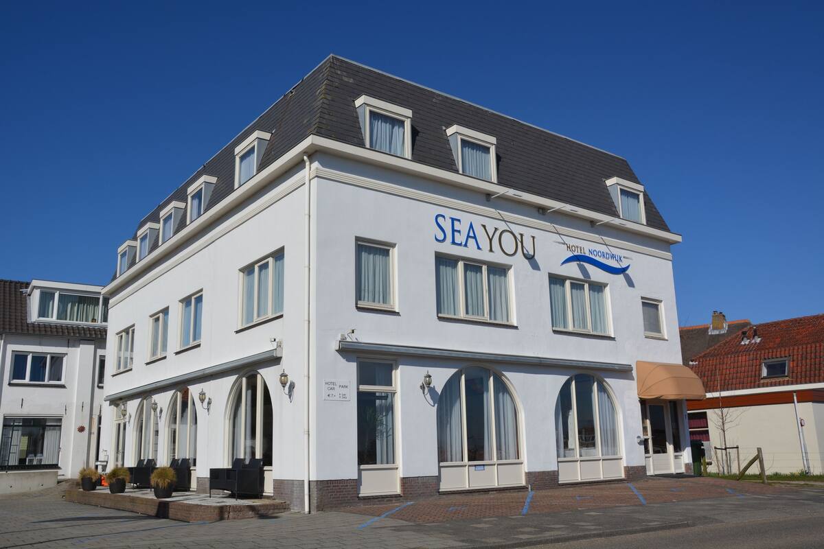 A hotel named "SEAYOU" with a white facade, large arched windows, and a parking area in front.