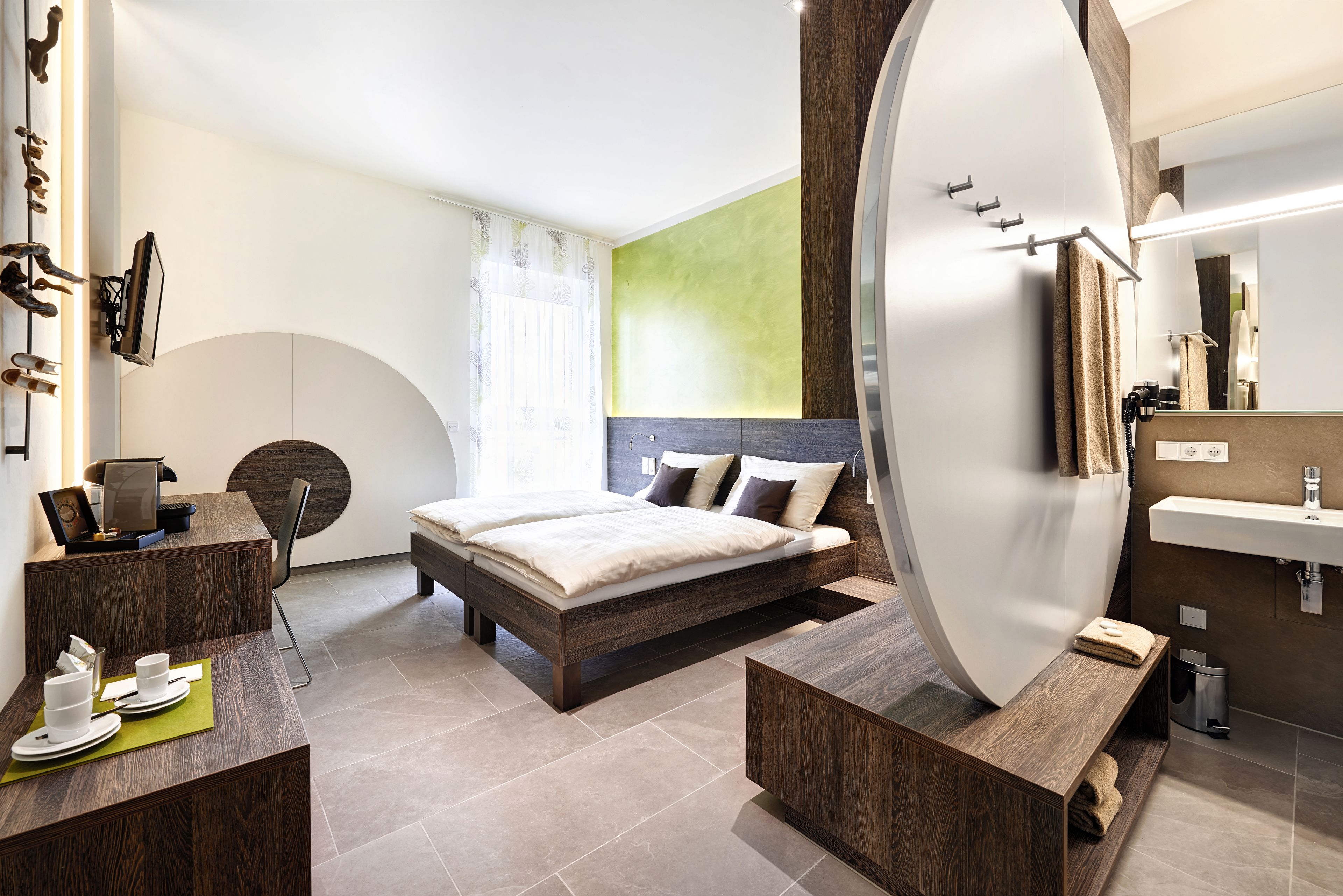 A modern hotel room with a bed, a desk, a mirror, and a bathroom.