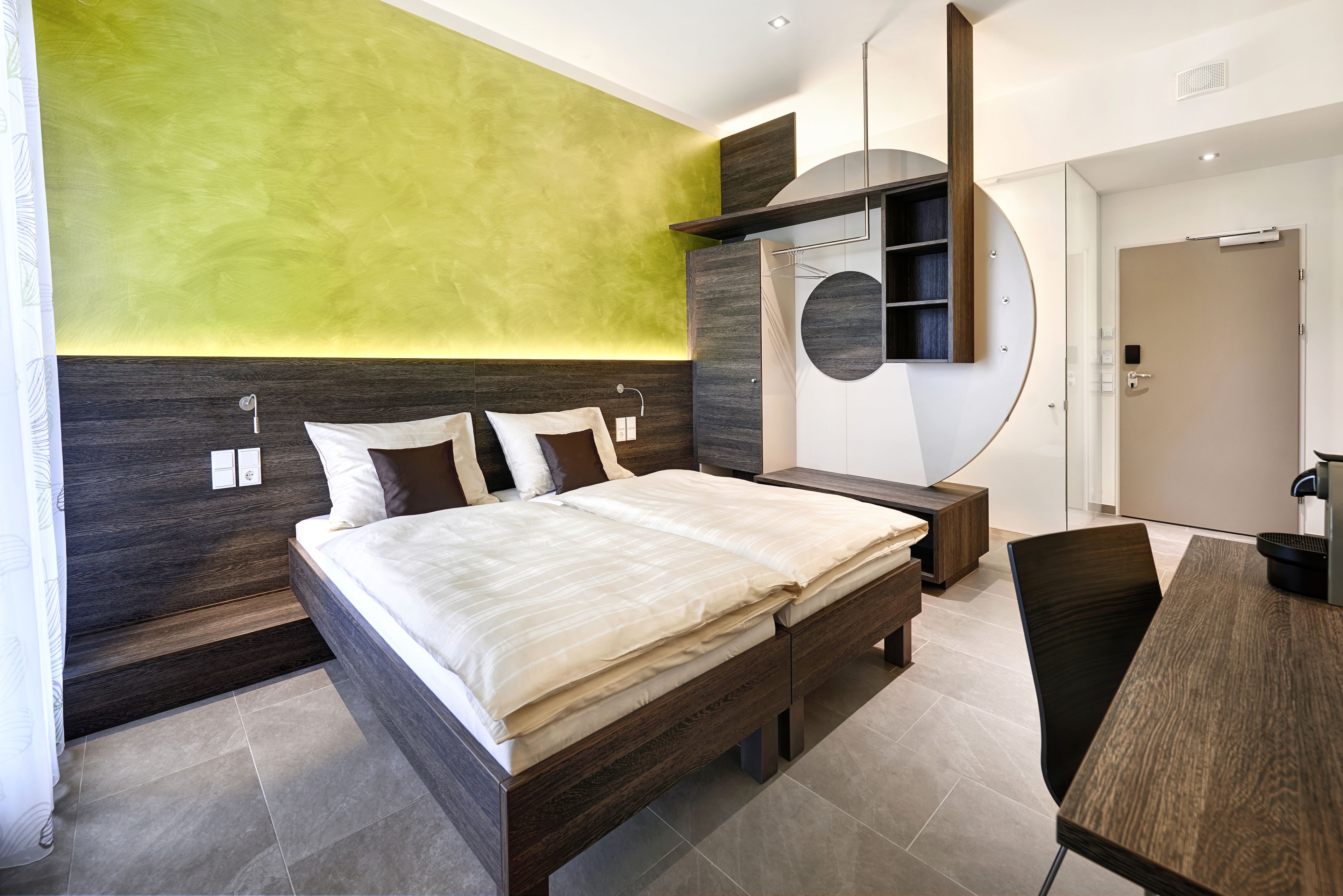Ein modernes Schlafzimmer mit einem großen Bett, einem Holznachttisch, einem runden Spiegel und einem eingebauten Kleiderschrank.