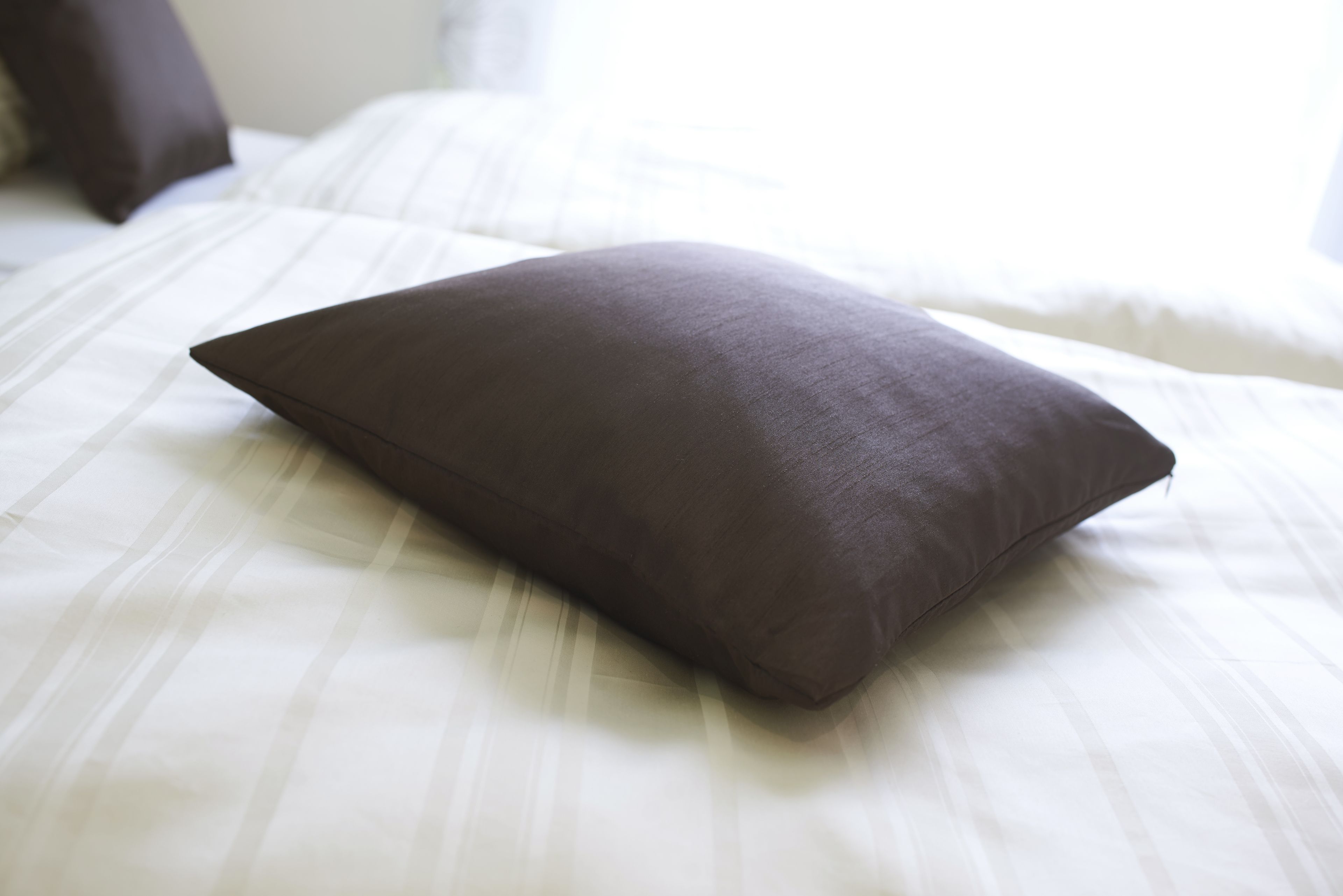 A bed with white bedding and a single dark-colored pillow.