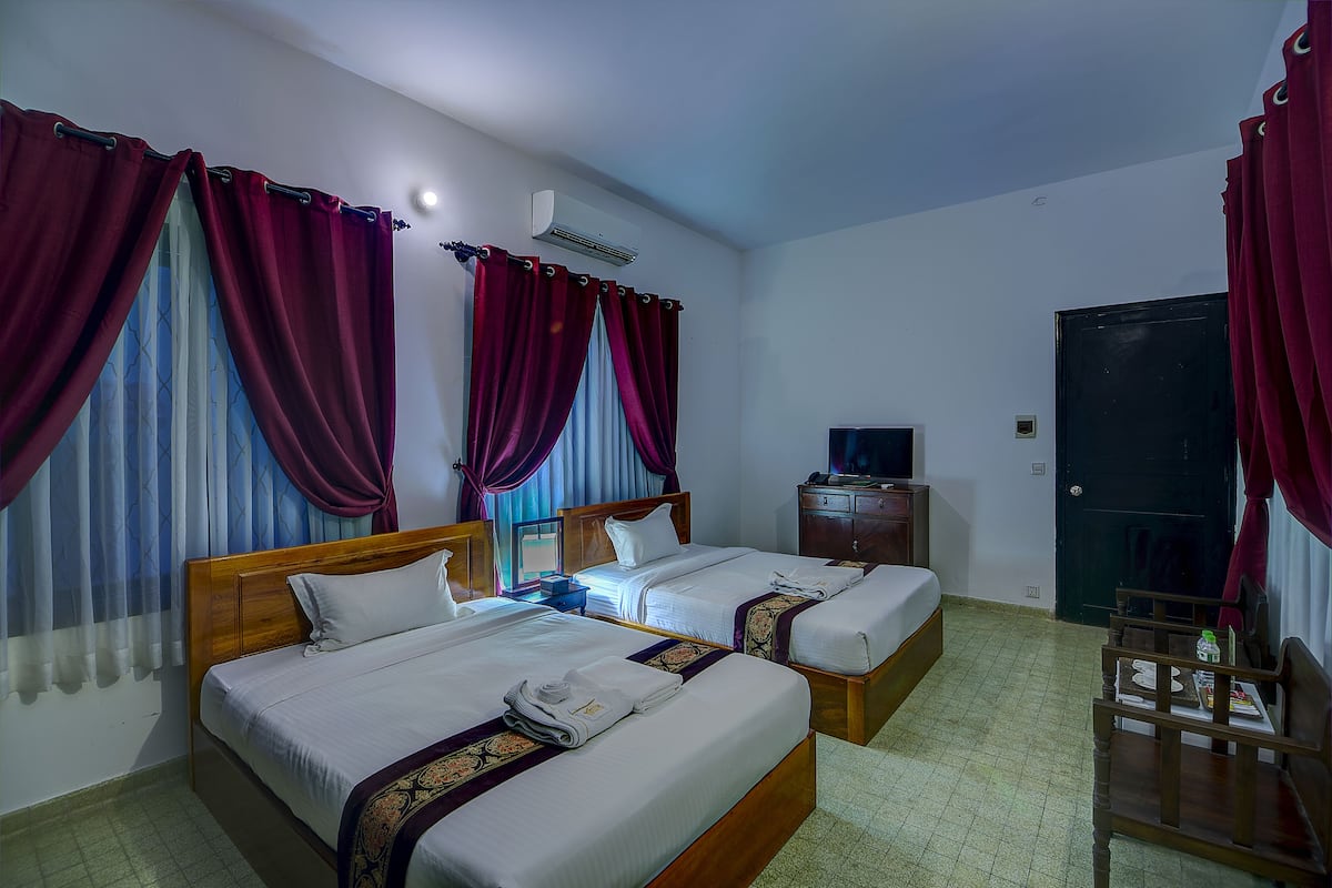 A hotel room with two beds, a TV, a wardrobe, and a desk.