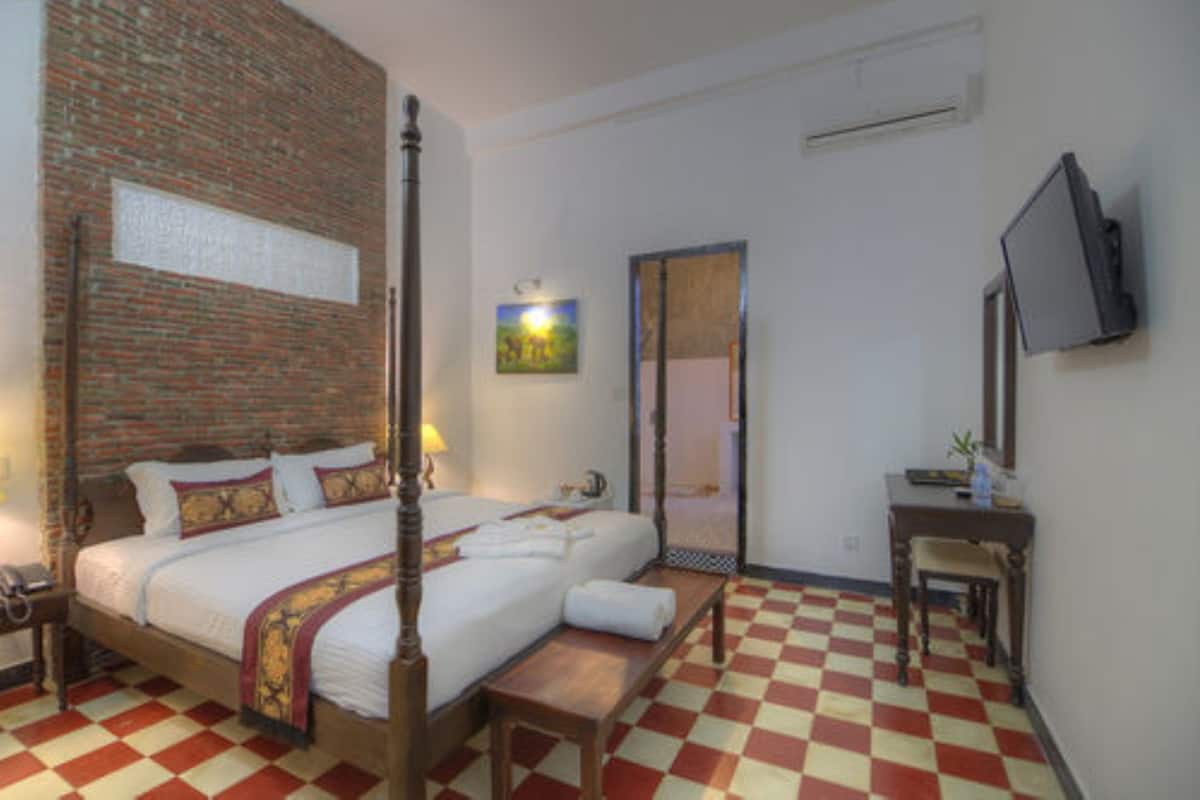 A hotel room with a checkered floor, a four-poster bed, a flat-screen TV, and a small table with a chair.