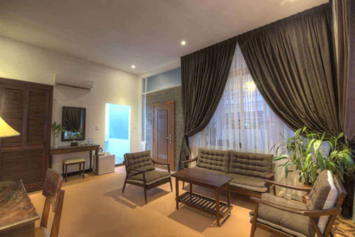 A living room with a sofa, armchairs, a coffee table, and a dining table. There is a window with curtains, a door, and a plant.