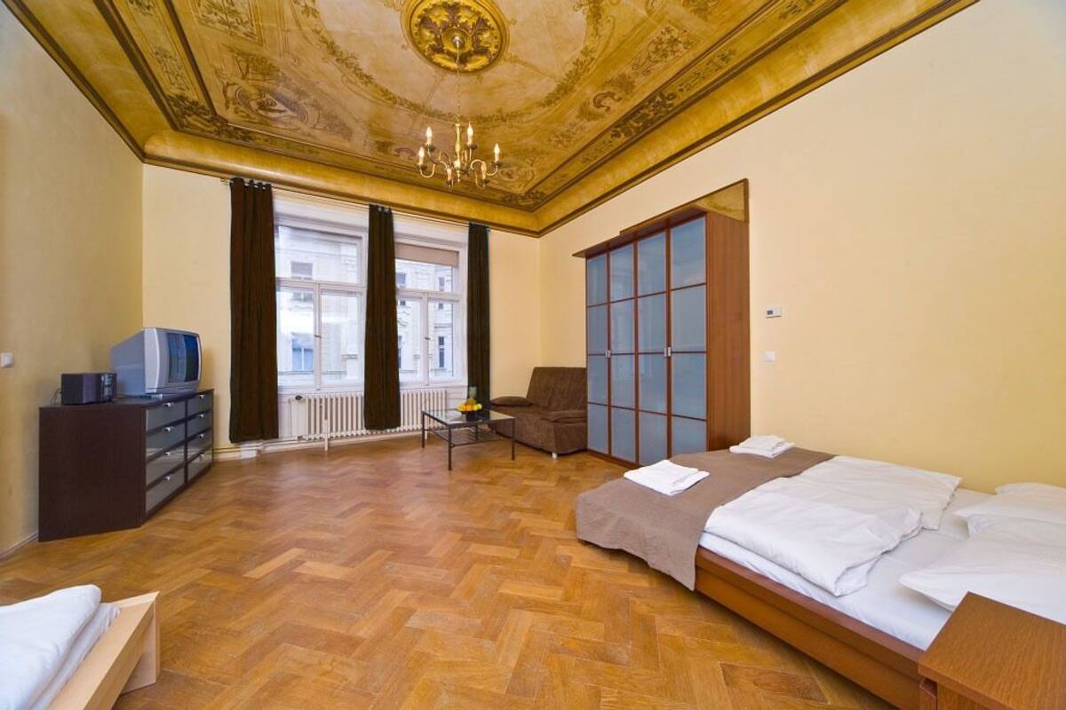 Habitación de hotel con piso de parquet de madera, una cama, un sofá, un televisor sobre un mueble y vistas de la ciudad a través de amplios ventanales.