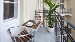 Un balcón con una mesa para dos personas, una planta en maceta y vista al interior del edificio.
