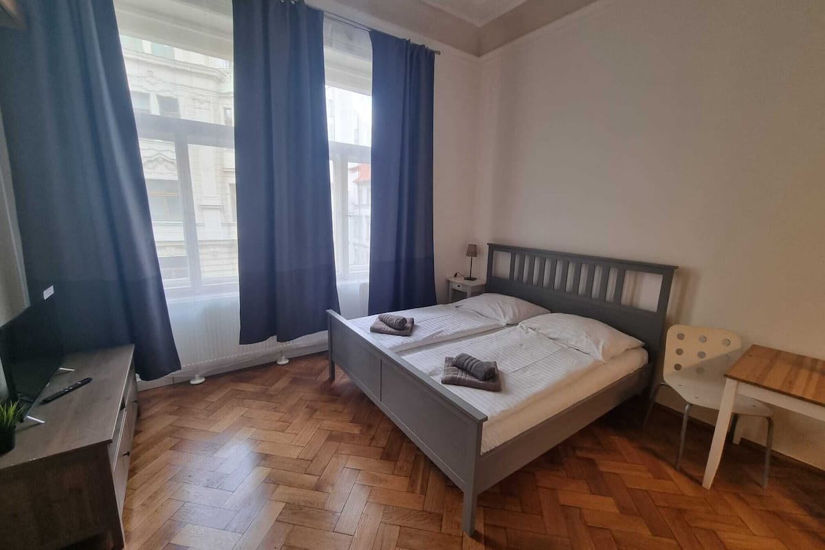 Un dormitorio con cama, escritorio, silla y ventana con cortinas.