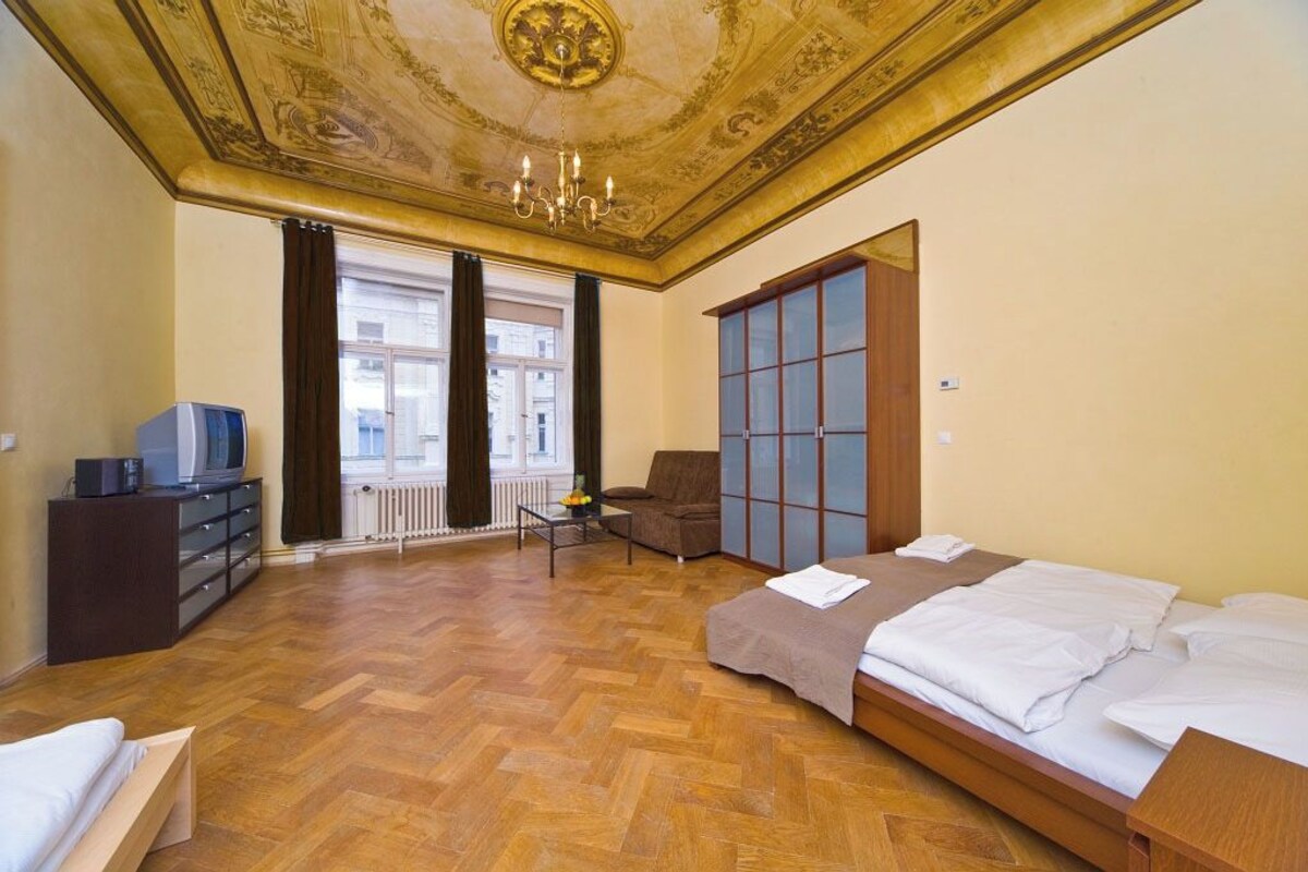 Habitación de hotel con piso de madera, cama, sofá, televisión y vista a la ciudad a través de amplios ventanales.