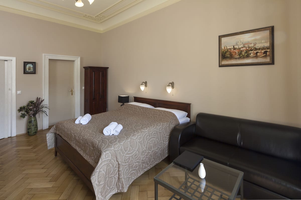 Una habitación de hotel con una cama, un sofá de cuero negro, una mesa de centro de vidrio y un cuadro en la pared.