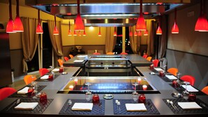 A restaurant with a long table set for dining, red pendant lights, and a modern interior design.