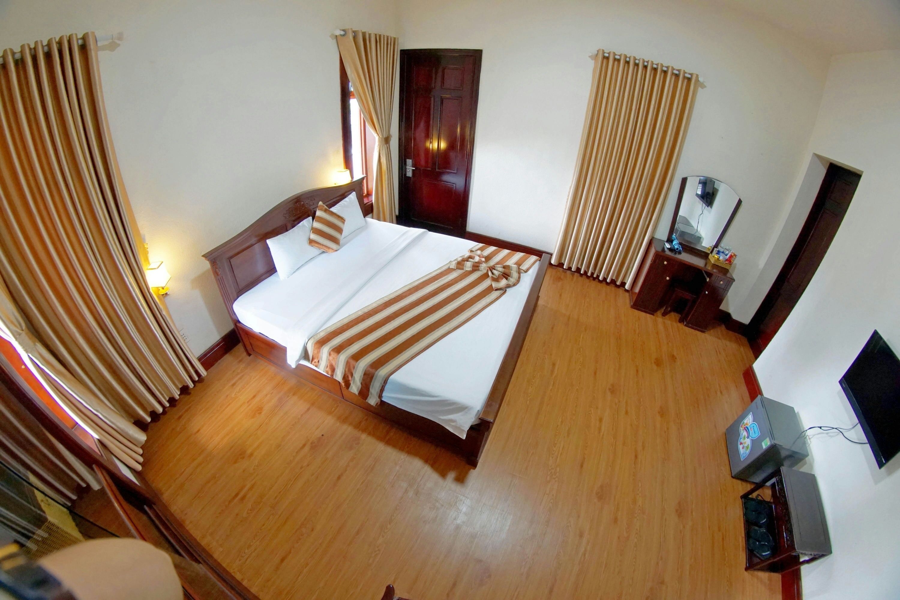 A hotel room with a large bed, wooden flooring, a desk with a computer, and a mirror.