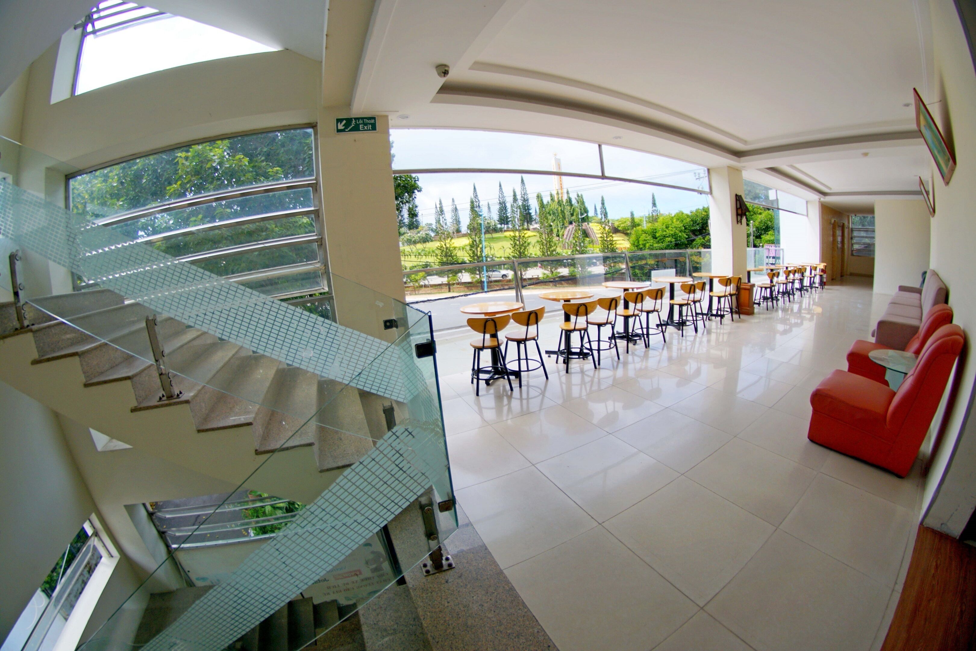 A multi-level indoor space with a glass staircase, a dining area with tables and chairs, and a red seating area.