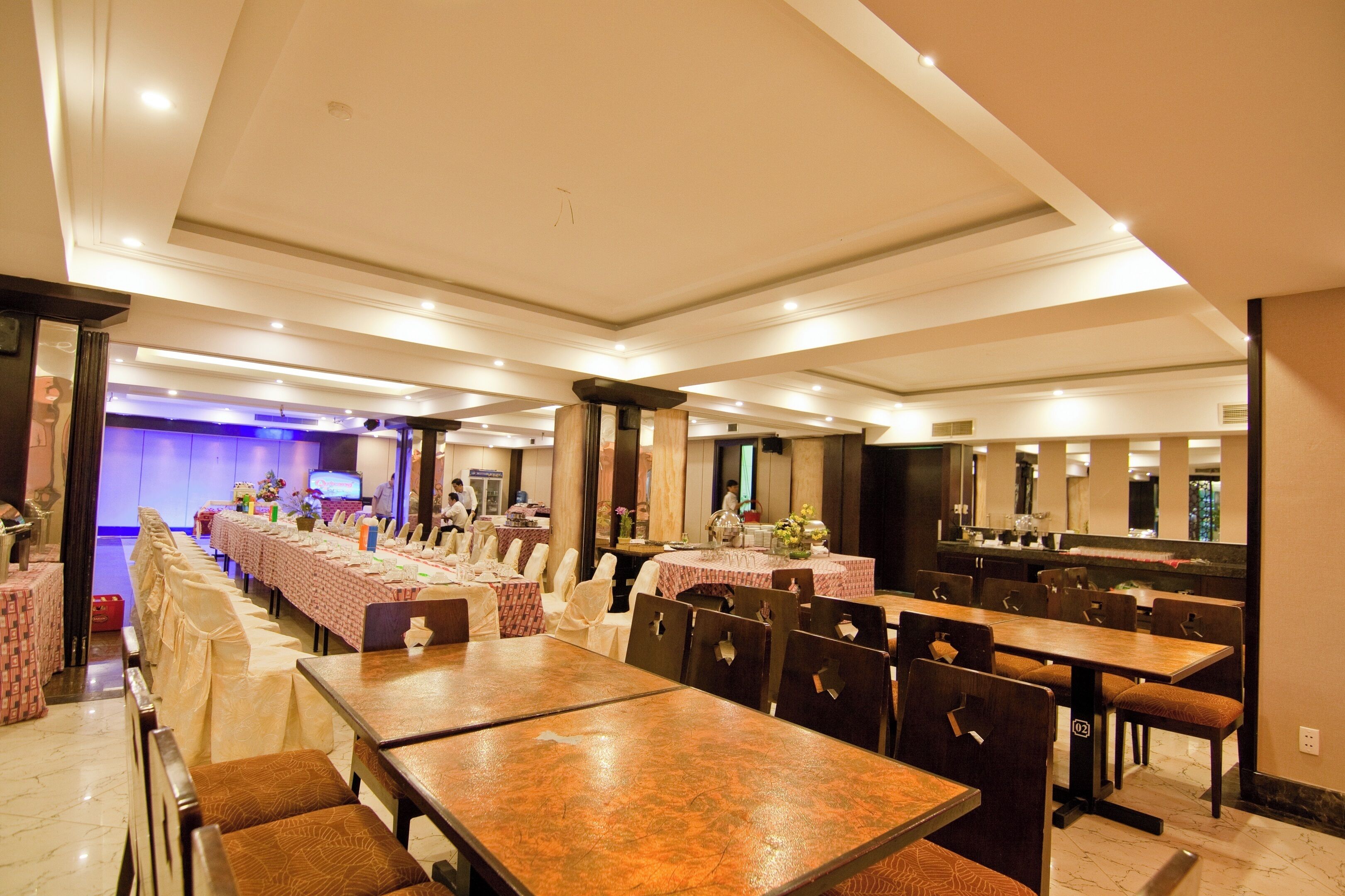 Une salle de banquet spacieuse, avec de longues tables et des chaises, une scène en arrière-plan et un design moderne au niveau du plafond.