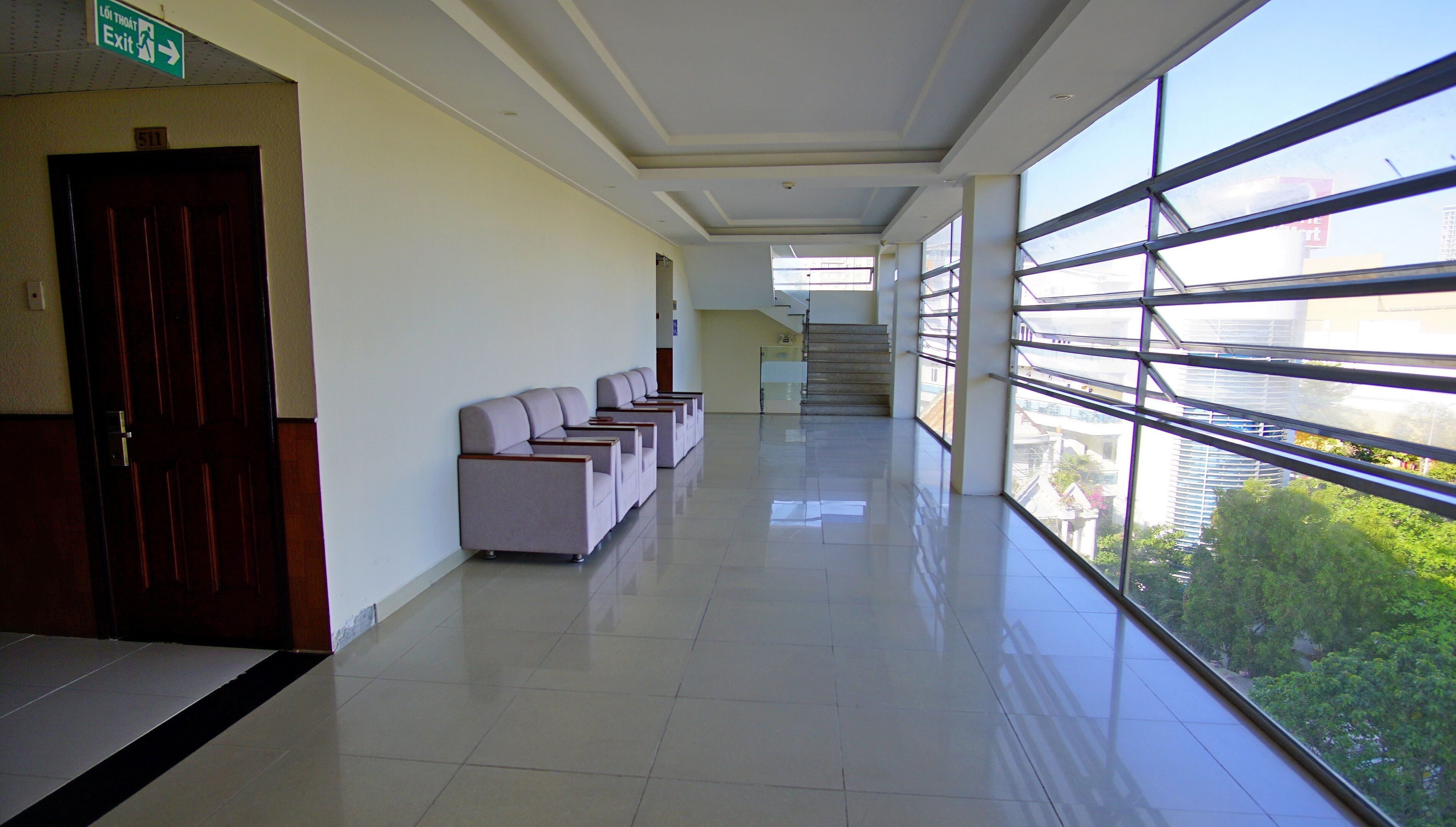 A spacious hallway with a row of seating, a staircase, and large windows offering a view of the city.
