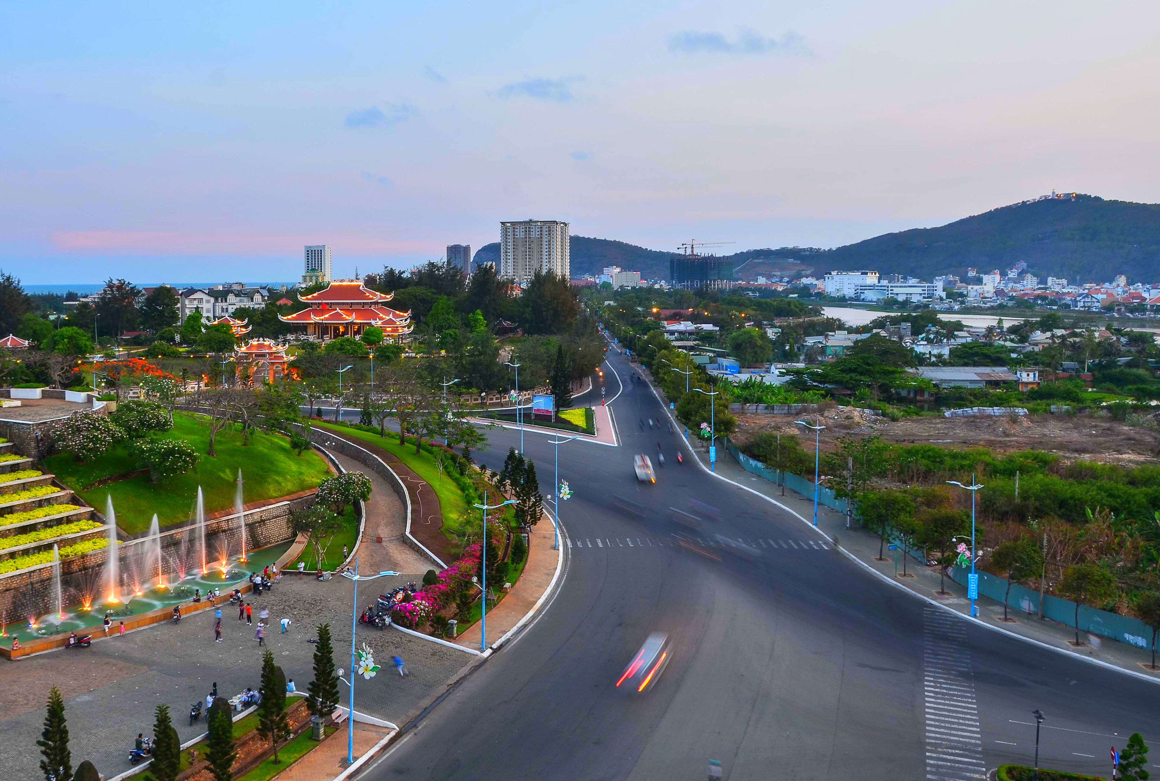 A wide road with a curved sidewalk and a fountain area.