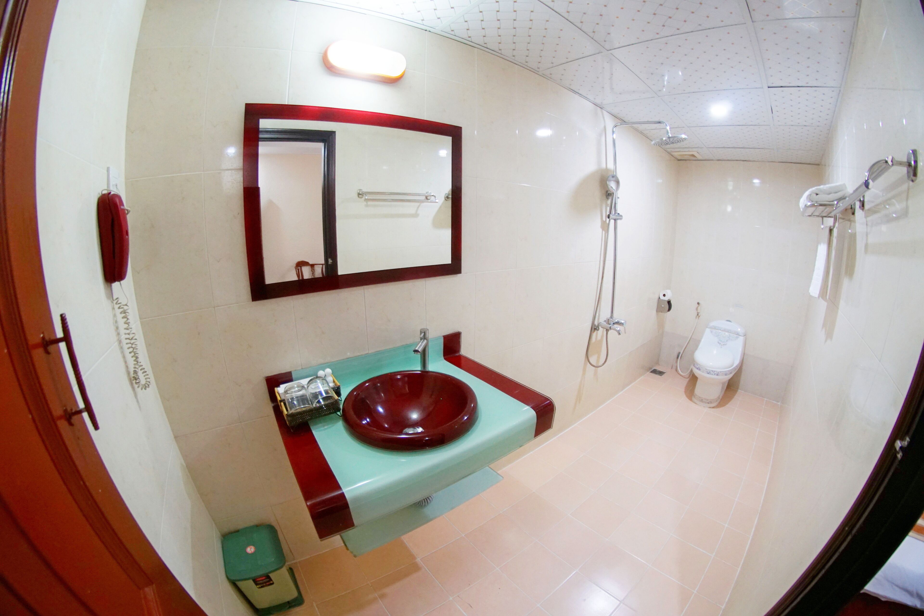 A bathroom with a red sink, a mirror, a shower, and a toilet.