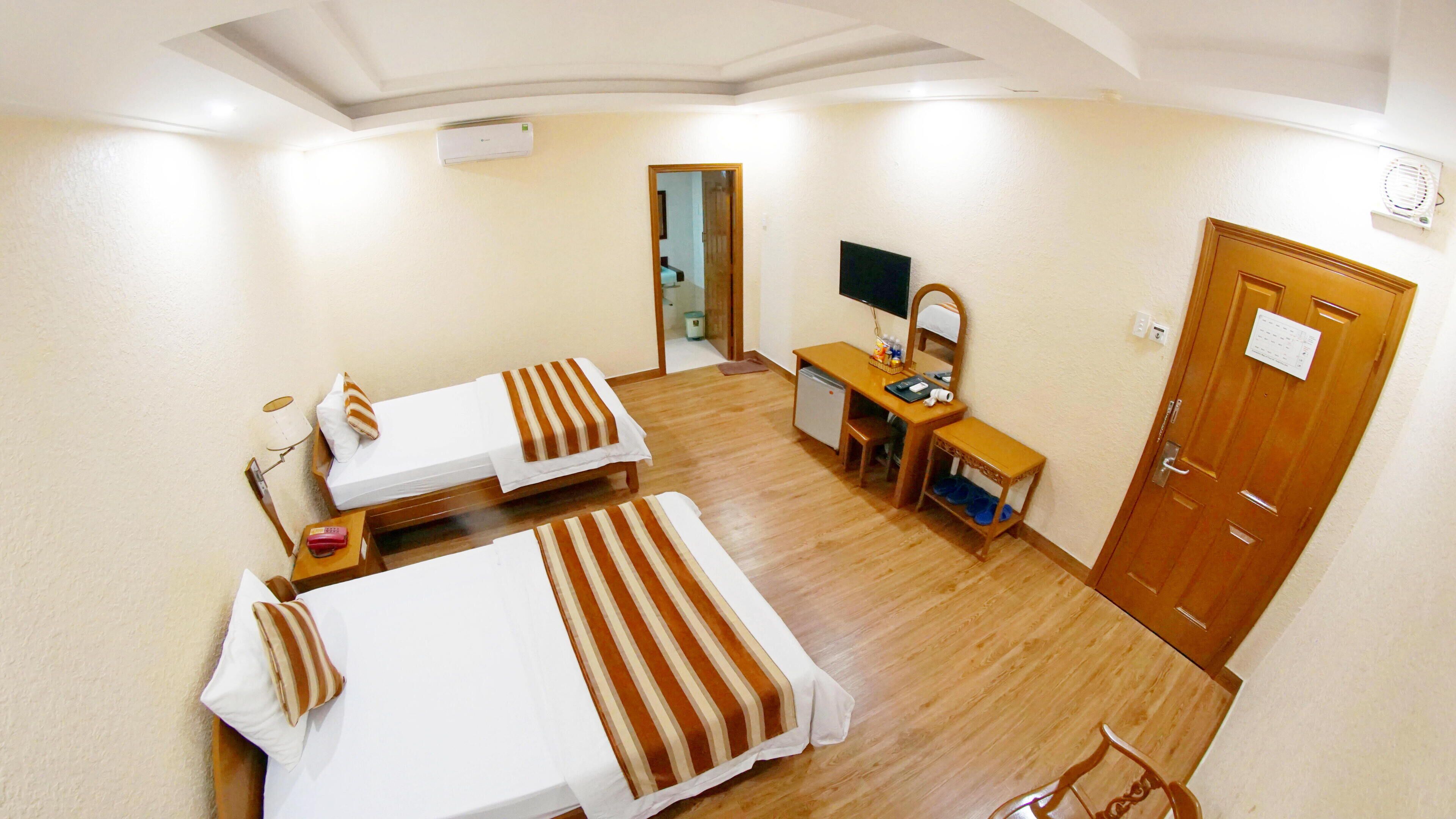 A hotel room with two beds, a desk with a chair, a small table, a TV, and a door.