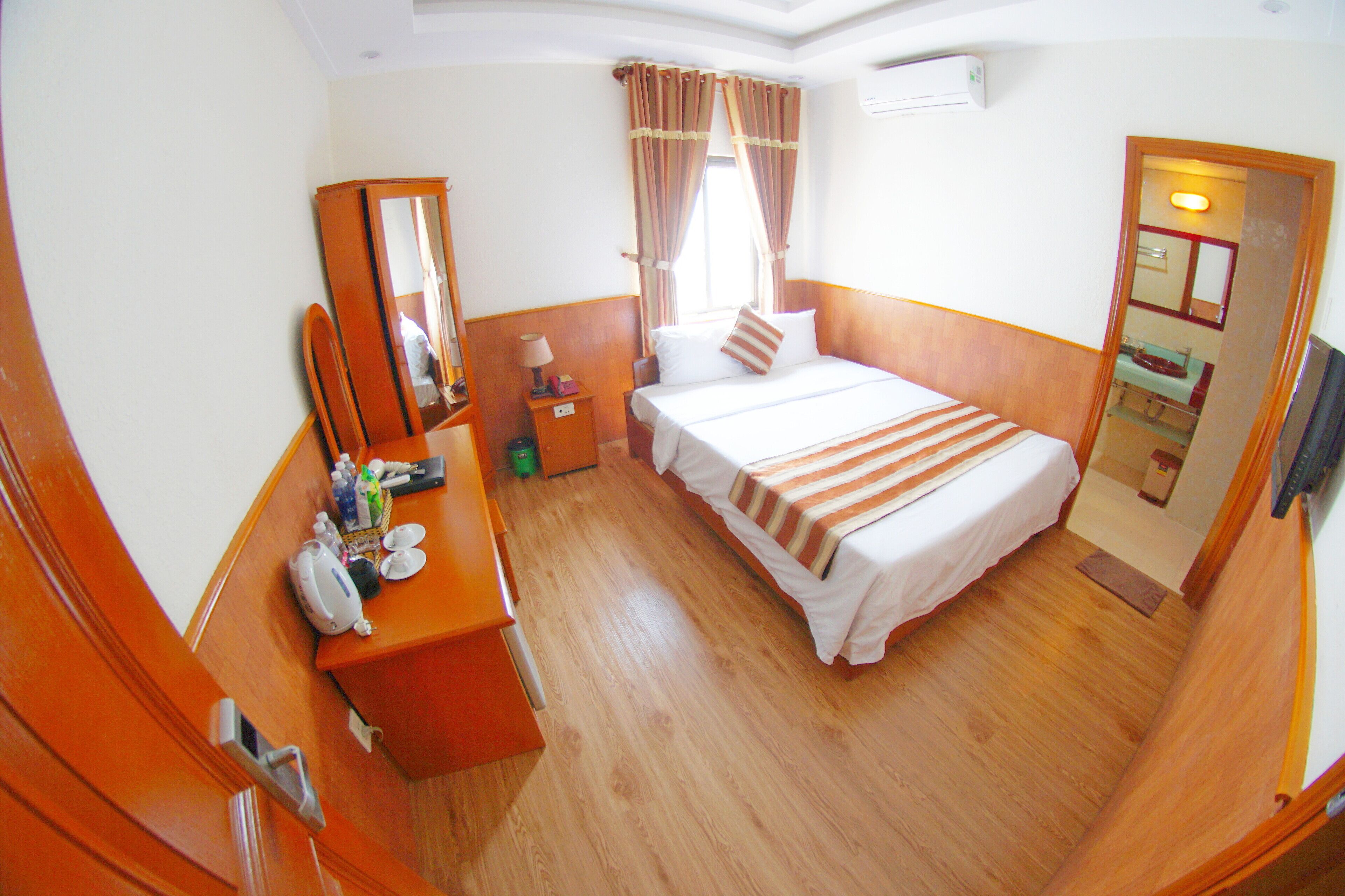 A hotel room with a bed, a desk with a mirror, a dresser, and a bathroom visible through an open door.