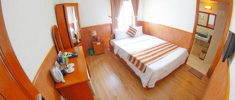A hotel room with a bed, a desk with a mirror, a dresser, and a bathroom visible through an open door.