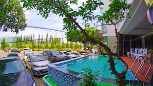 Una piscina con borde de azulejos, rodeada de coches aparcados y un árbol.