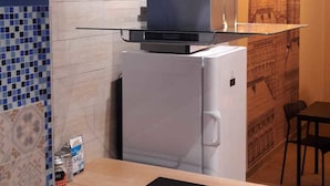 A compact kitchen with a white refrigerator, a black induction cooktop, and a blue-tiled backsplash. - Hostel Melting Pot Rome (Rome)