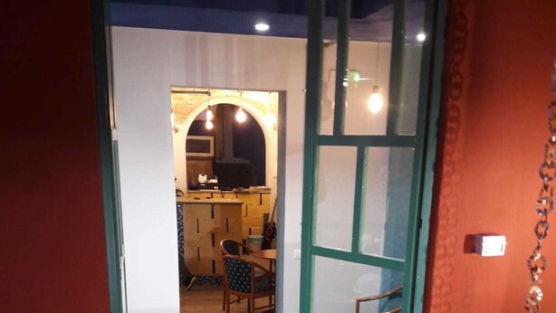 A wooden bench leading to a room with a green-framed door, a kitchen area with a dining table and chairs, and a small outdoor seating area with a metal chair. - Hostel Melting Pot Rome (Rome)