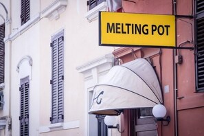 A yellow sign with "MELTING POT" written on it, attached to a building with a beige facade and black shutters. - Hostel Melting Pot Rome (Rome)