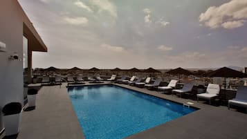 A rooftop pool with lounge chairs and umbrellas, surrounded by a cityscape.