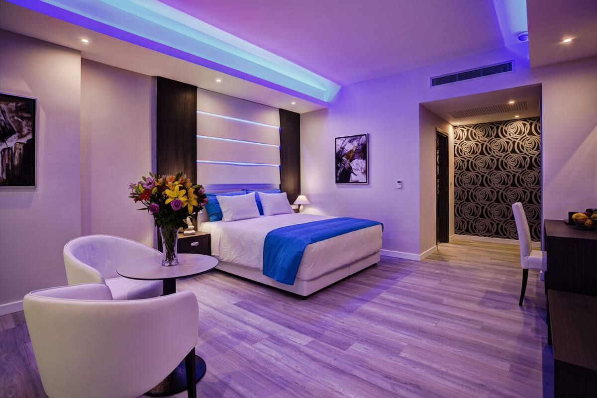 A modern bedroom with a bed, bedside tables, a chair, and a small table with a vase of flowers.