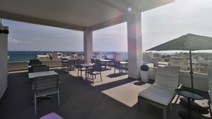 Una terraza en la azotea con mesas y sillas, una sombrilla y vistas al mar.