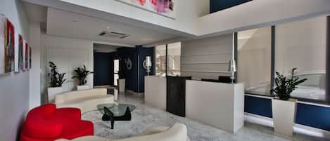 A modern living room with a sofa, a glass coffee table, and a red accent chair. There is a kitchen area with a sink and a countertop.