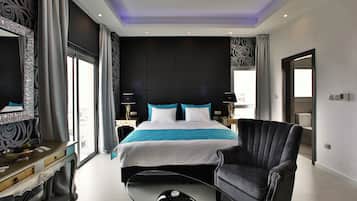 Habitación de hotel moderna con una cama grande, un sillón negro, una mesita de centro de vidrio y un espejo amplio.
