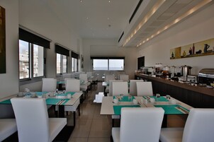 A modern dining area with tables and chairs, a buffet counter, and large windows offering a view.
