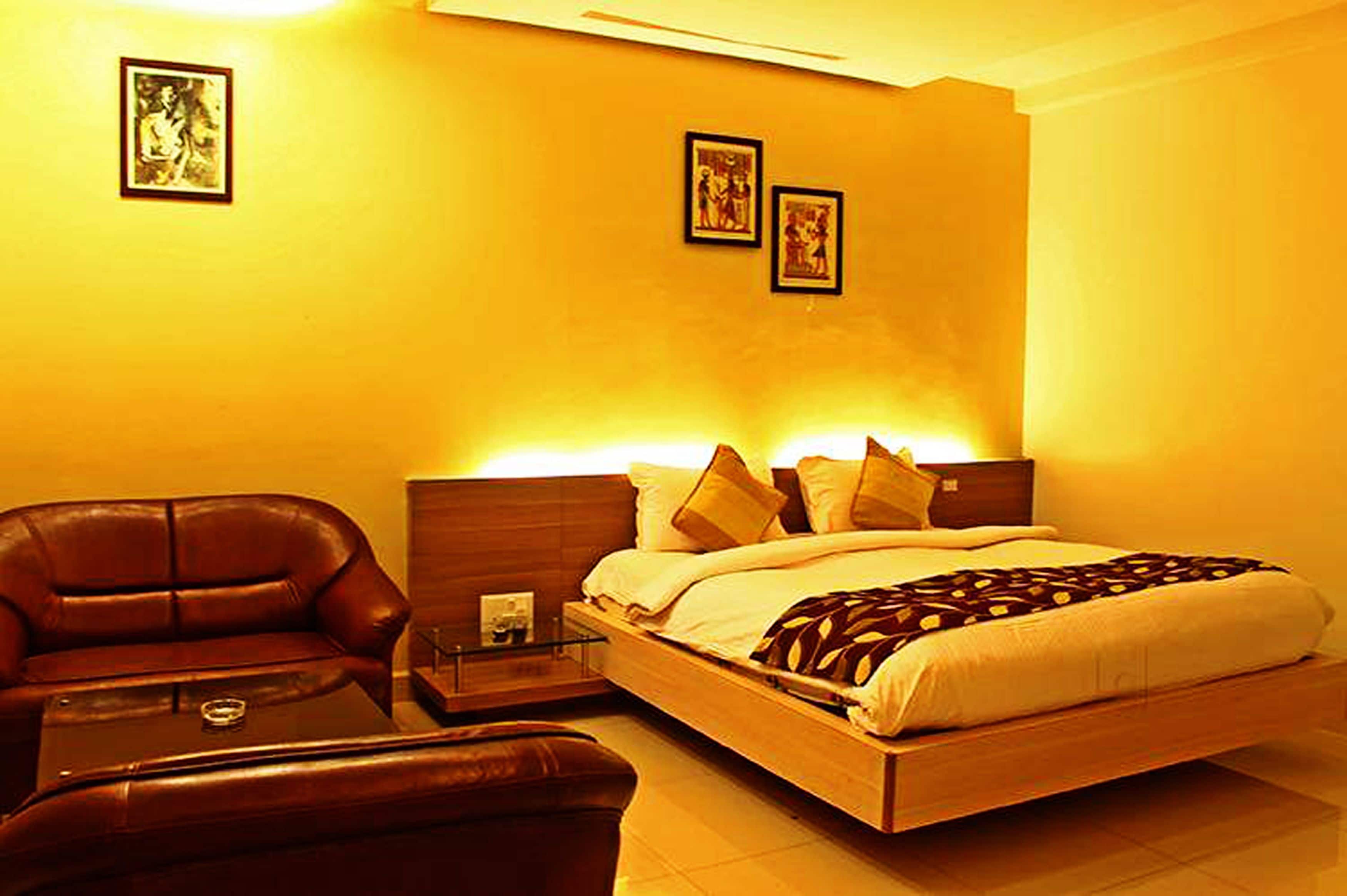 A hotel room with a bed, a leather armchair, a small table, and two framed pictures on the wall.